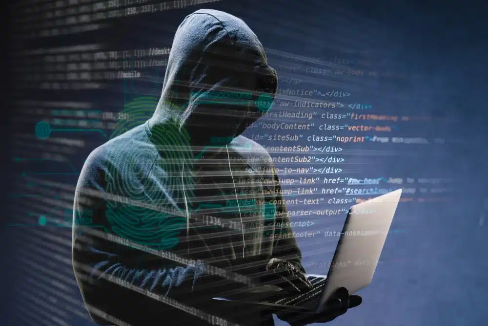 A hooded figure holding a laptop, surrounded by lines of code and digital symbols, representing a hacker