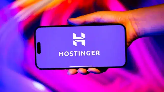 Hand holding a smartphone displaying the Hostinger logo.
