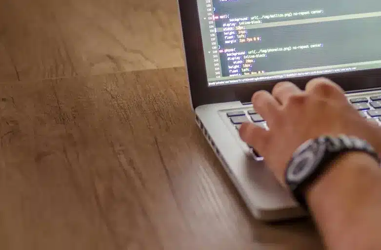 A person typing code on a laptop, with lines of HTML and CSS visible on the screen.