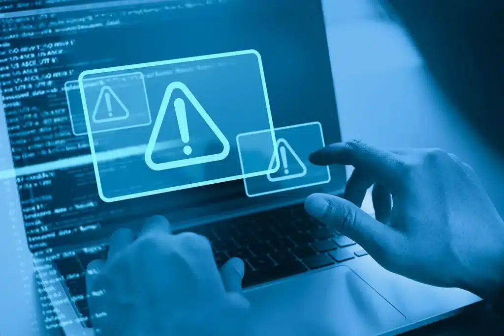 Hands using a laptop with warning alerts indicating a cyber security threat.